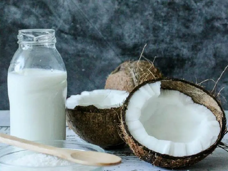 Leite de coco em uma garrafa ao lado de um coco aberto